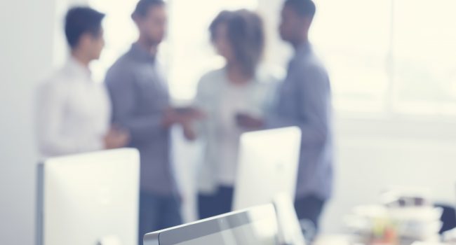 Defocussed image of 4 people working on a digital tablet. Multi cultural group with African, mixed race, Asian and Caucasian ethnic groups represented. They are standing together looking at a digital tablet. Contemporary style intended for use as a background with copy space.