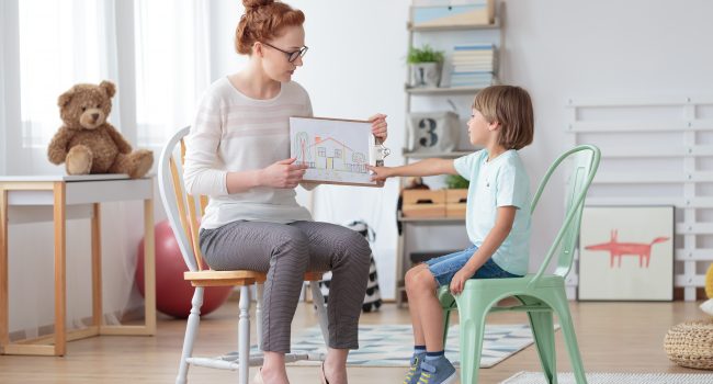 Professional family counselor helping young child to cope with parents' divorce showing to little boy a drawing of house